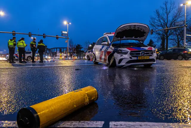 Beschadigde politieauto op een nat kruispunt