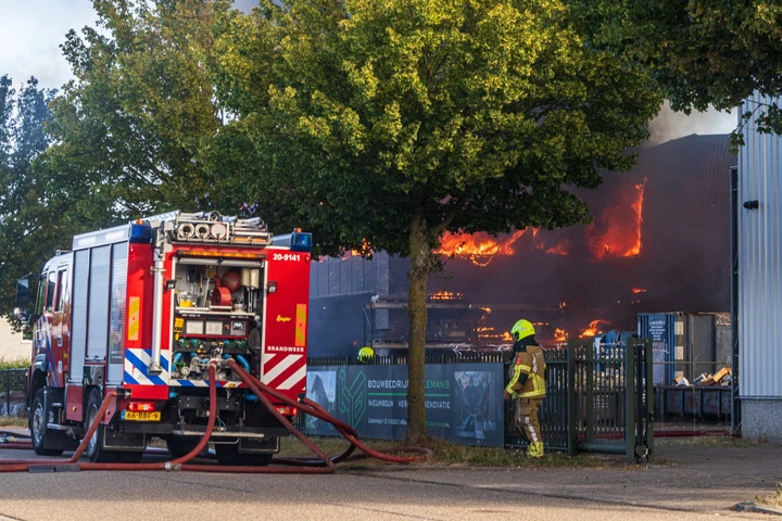Brandweervoertuig en brandslangen bij een brandend bedrijfspand in Udenhout