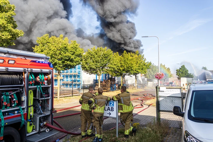Brandweerlieden bij voertuigen tijdens een zeer grote industriebrand in Udenhout