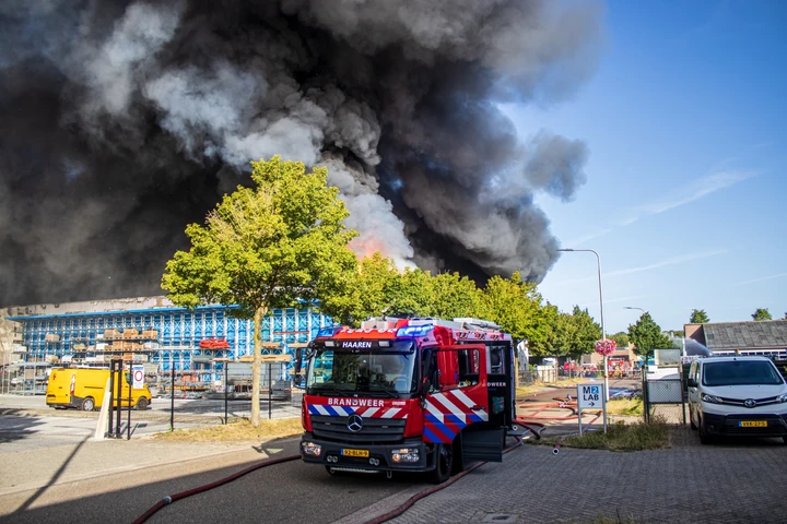 Grote rookwolken boven een industriebrand in Udenhout met een brandweervoertuig op de voorgrond