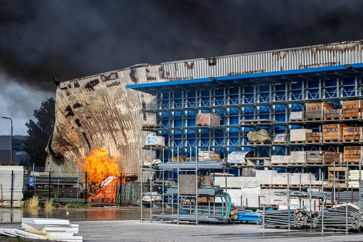 Vlammen langs een beschadigde gevel tijdens een grote industriebrand in Udenhout
